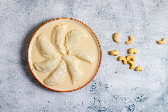 Traditional Bengali dudh puli pitha features rice flour dumplings stuffed with coconut and jaggery, gently simmered in sweetened milk, rich, comforting winter dessert.
