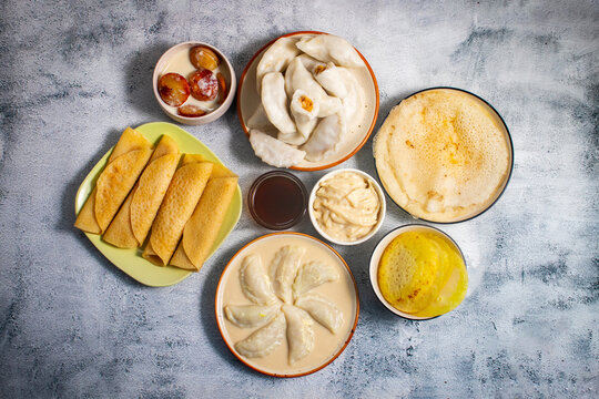 Traditional Bengali pitha platter featuring patisapta, bhapa puli, dudh puli, chakuli, sweet sauces, milk, coconut jaggery fillings, arranged neatly on rustic background.
