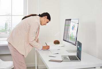 Businesswoman accountant reviews finance charts at computer. She audits numbers in a modern office, accounting entries and verifying the report. Clear view of financial analysis and audit.
