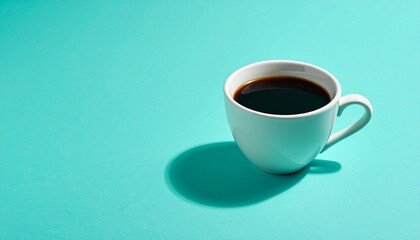 Fototapeta premium White ceramic cup of black coffee casting shadow on turquoise surface.