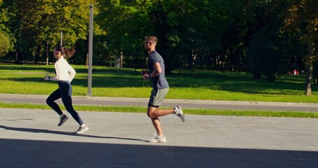 Obraz premium A young man and a woman run at speed in a city park on a summer day