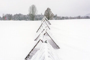 Snow-Covered Metal Snow Fences in Winter Landscape. Winter landscape with snow-covered metal snow fences stretching across a frozen field, close to the village.