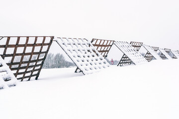A winter landscape with snow-covered windbreak fence for snow stretching across a frozen field near the village, with a traffic sign visible in the background.