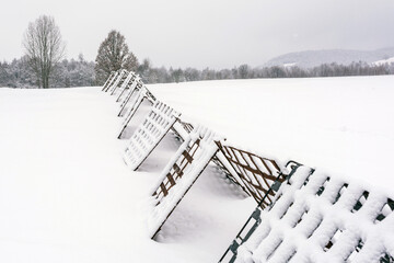 Snow-Covered Metal Snow Fences in Winter Landscape. Winter landscape with snow-covered metal snow fences stretching across a frozen field, close to the village.