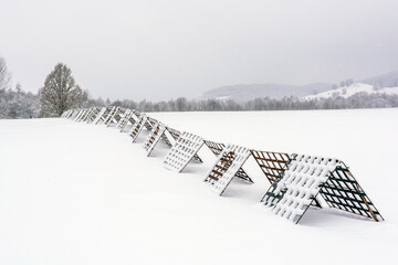 Snow-Covered Metal Snow Fences in Winter Landscape. Winter landscape with snow-covered metal snow fences stretching across a frozen field, close to the village.