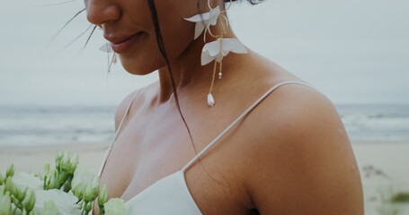 The bride smiles looking at the bouquet standing on the seashore, close-up, the video moves from the face to the flowers