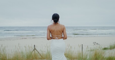 The groom approaches the bride standing on the seashore backwards, they embrace