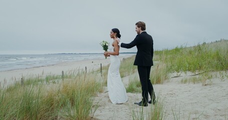 The groom approaches the bride standing on the seashore with her back to him, they embrace