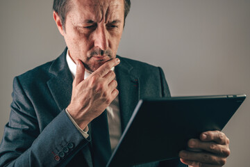Thoughtful businessman in suit holding tablet with hand on chin