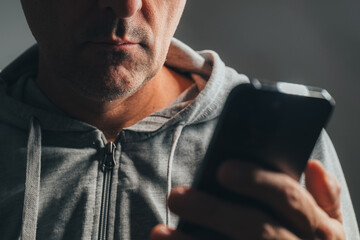 Closeup of casual man using smartphone, only lower face visible with mouth and chin in focus and part of phone blurred in foreground.