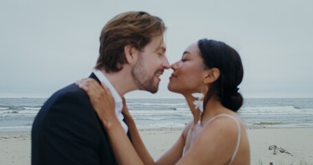 The bride and groom rub their noses and kiss standing on the seashore