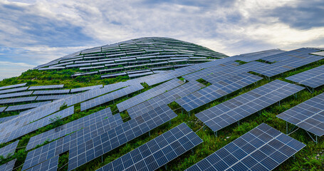 Sustainable solar panel farm installed on a lush green hill under a cloudy sky.