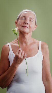 Elderly woman posing with a flower in the studio, vertical video
