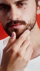Naklejka premium Young man touching his beard while looking at camera while standing against monochrome studio background, vertical video