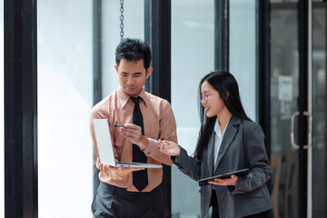 Asian business professionals discussing project data using a laptop and tablet, fostering teamwork and modern collaboration in a corporate setting