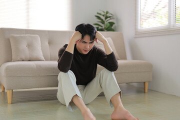 Asian man feeling frustrated and stressed while sitting on the floor at home, experiencing depression and loneliness
