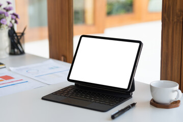 Modern tablet with empty white screen and keyboard on a clean workspace, surrounded by business documents and a coffee cup