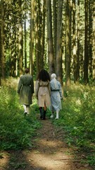 Fototapeta premium Three women with different hair colors walk through the forest, rear view, vertical video