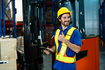 Male adult caucasian logistics worker wearing safety vest and helmet holding tablet while checking inventory beside wrapped packages at modern warehouse facility, inside logistics warehouse.