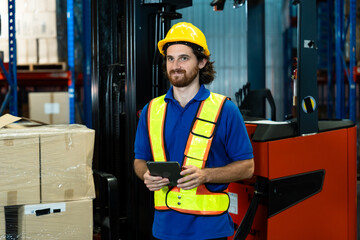 Warehouse worker using digital tablet standing near stacked packages and forklift inside organized storage center during inventory check operation in logistics department, inside logistics warehouse.