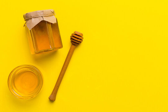 Glass jar of honey with wooden drizzler on colored background. Honey pot and dipper high above. Top view copy space