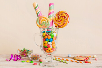 Fototapeta premium Colorful candies in cup on table on light background background. Large swirled lollipops. Creative concept of a jar full of delicious sweets from the candy store