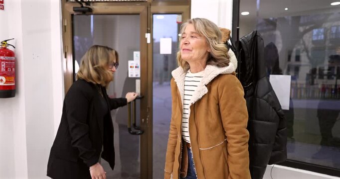 Polite young employee holding the glass door open for a happy mature woman entering the office building, showing respect and good manners between different generations of coworkers