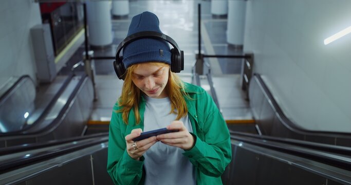 A woman plays an online game on a smartphone while going up the escalator in the subway