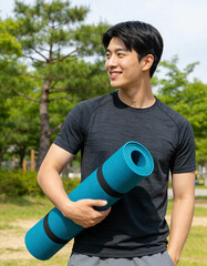 Young Asian man holding yoga mat in the park. Healthy lifestyle concept.