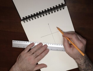 The coordinate system axis is drawn in a notebook, hands are holding a metal ruler and a pencil, at a brown table