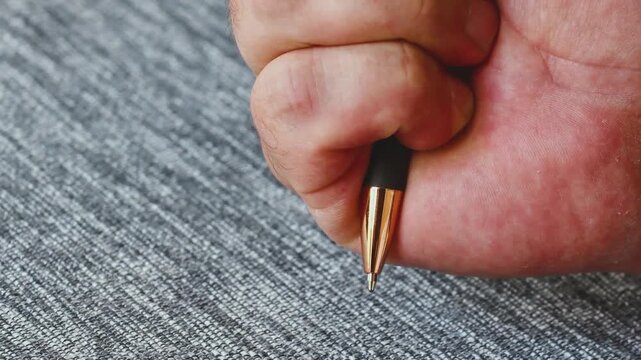 Close-up view of a man pressing a push button ballpoint pen while resting on a textured surface