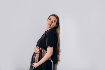 Naklejka premium Young beautiful pregnant woman model with long hair in a beautiful black dress, in the studio