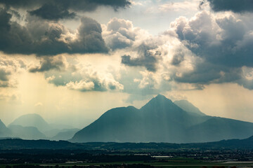 Dramatic mountain silhouette with sunbeams shining through storm clouds over valley