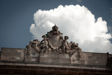Stone coat of arms with imperial crown and cherubs on the roof of Hofburg Palace in Vienna against cloudy sky
