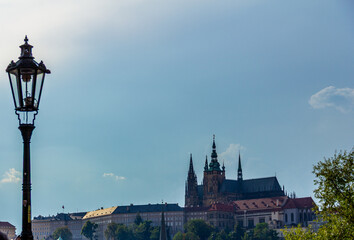 Vintage street lamp with St. Vitus Cathedral and Prague Castle complex in background against blue sky