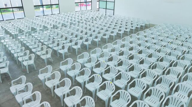 Wide cinematic view of an empty modern event hall filled with neatly arranged white plastic chairs, symbolizing scale, organization, and anticipation before a large conference or public gathering.
