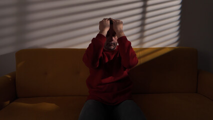 Man with headache, depression, sadness and loneliness sitting on a couch at home