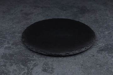 Round rustic black slate stone plate, on stone background