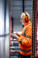 Senior industrial worker wearing safety equipment reviewing tablet data