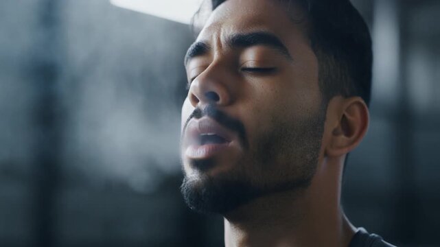 Post-Set Deep Breath. Fitness Resolutions - High-Intensity Training & Athletic Ambition. A man taking a deep breath after a maximal set eyes closed condensation rising from his mouth in the cool air.
