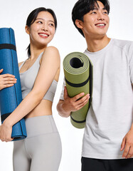 Young asian couple holding yoga mats and smiling at camera isolated on white background