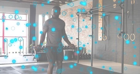 Skipping adult male wearing athletic shirt and shorts in fitness studio, showing jump rope and rig