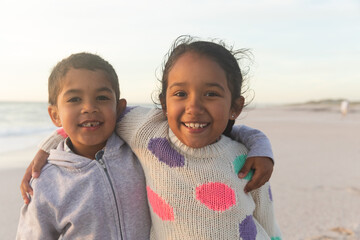 Portrait of smiling brother and sister standing with arms around at beach during sunset