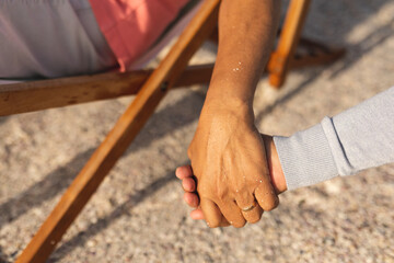 Cropped image of senior multiracial couple holding hands while enjoying retirement at beach