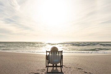 Retired senior woman sitting on folding chair relaxing at beach in front of horizon on sea