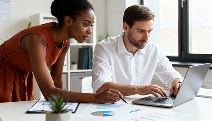 Diverse business colleagues analyzing financial data on a laptop in a modern office. Professional man and woman working together on a project with charts and graphs. Teamwork concept