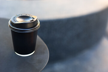 Minimal black takeaway coffee cup on a small round table with soft natural light and blurred background