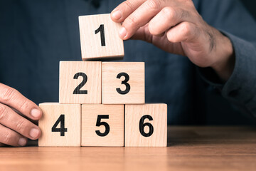 Man arranging wooden number blocks into a pyramid to represent step by step success, structured growth, and systematic progress concept for business strategy and personal career development