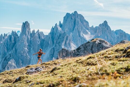 Woman trail running on a grassy mountain slope with jagged peaks