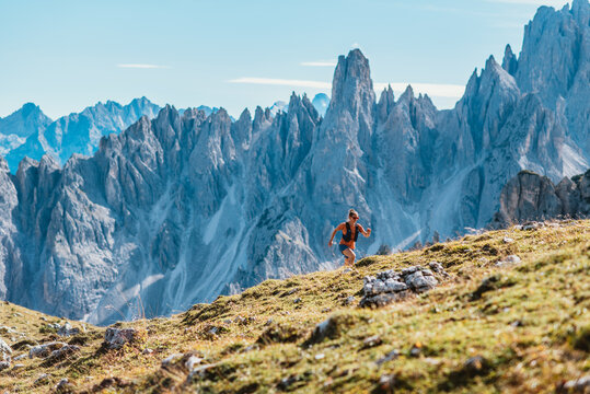 Woman trail running on a grassy mountain slope with jagged peaks